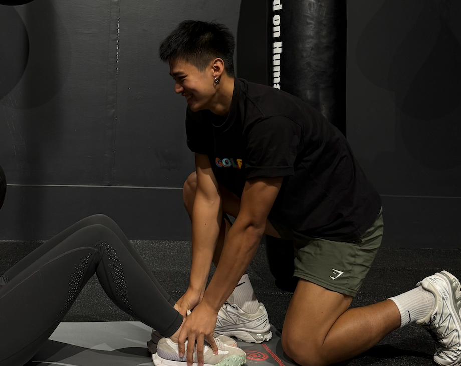A young man assists a person in workout gear during an exercise session, enhancing fitness training in a gym.